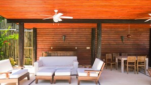 An outdoor patio with wooden furniture, including a sofa and chairs, under a wooden ceiling with ceiling fans. - Green Bamboo Cabana (Roatan)