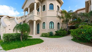 A multi-story building with a symmetrical facade, multiple balconies, and a paved courtyard with greenery.