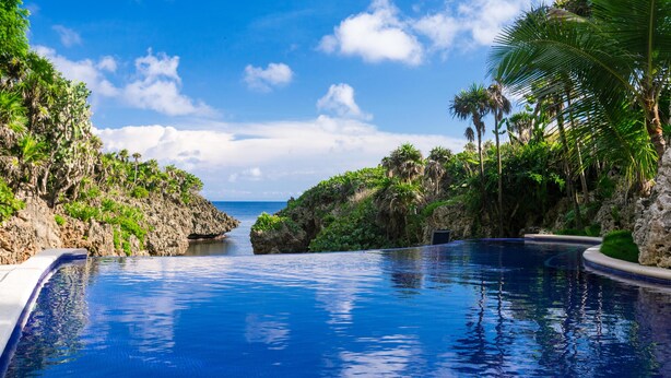 A clear blue pool with a view of the ocean and rocky cliffs.
