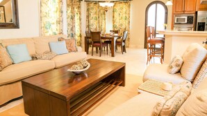 A spacious living room with a ceiling fan, a sofa set, a coffee table, and a dining area with chairs and a table.