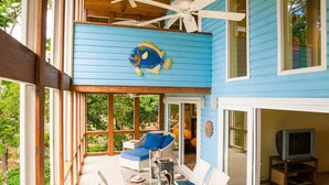 Une maison à deux étages dotée d’un balcon, d’un coin repas avec des meubles en osier blancs et d’un ventilateur de plafond.