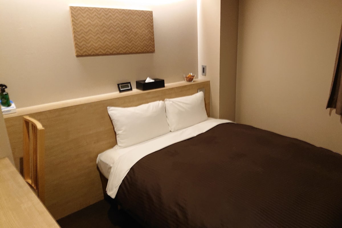 A hotel room with a bed, a headboard, a nightstand, a lamp, and a window with curtains.