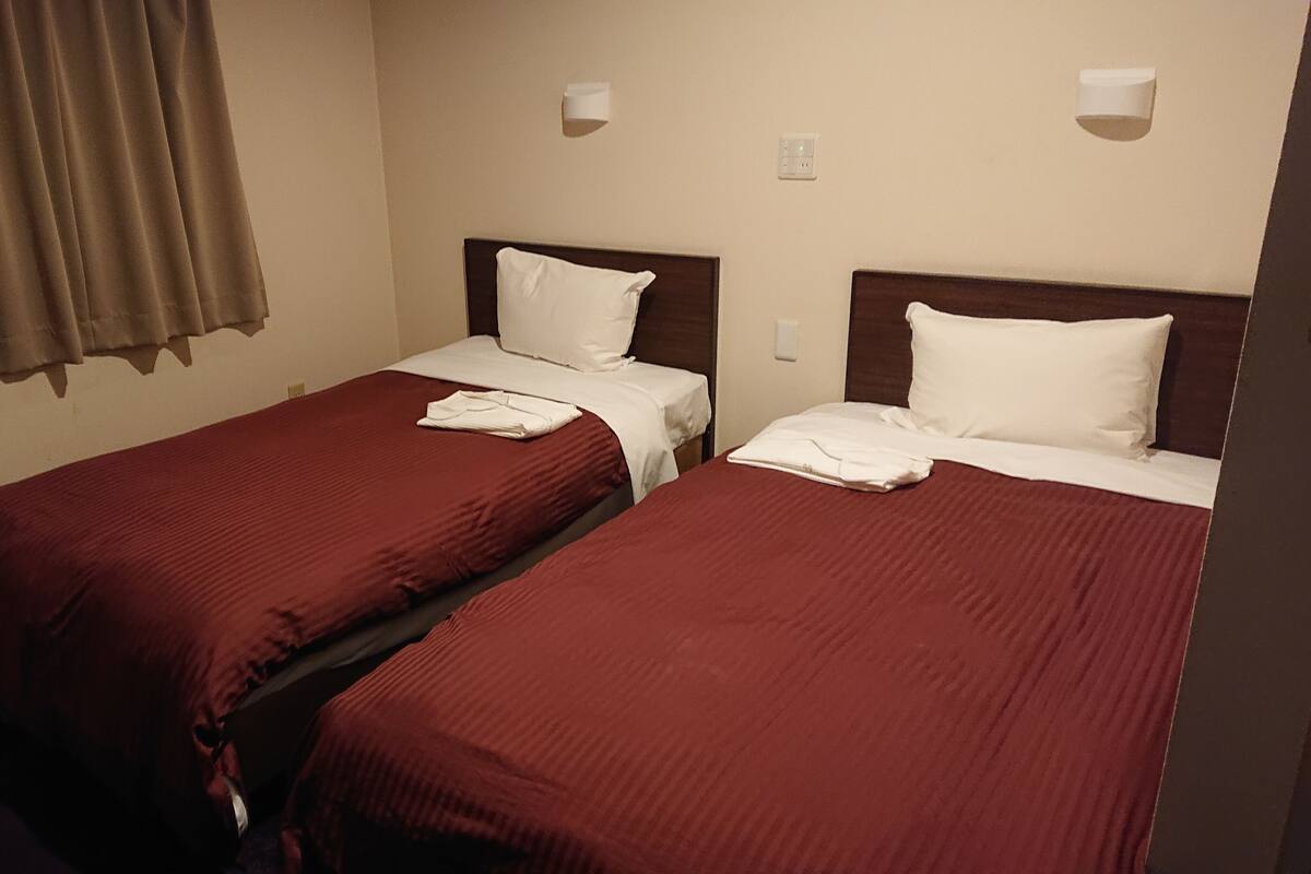 Two single beds with red bedding, white pillows, and folded towels.