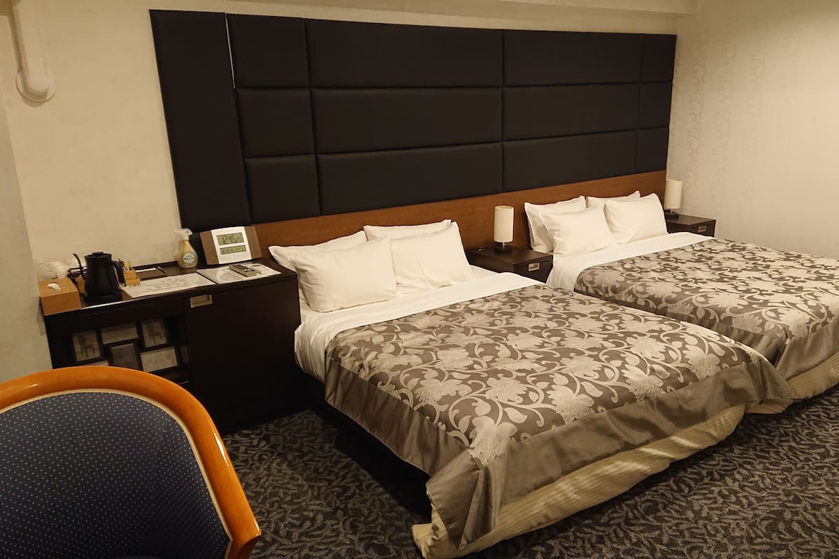A hotel room with two beds, a wooden headboard, a desk with a computer, and a chair.