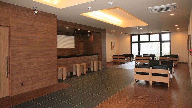 A modern waiting area with wooden benches, a reception desk, and large windows providing natural light. - Hotel Route Inn Natori Iwanuma Interchange (Iwanuma)