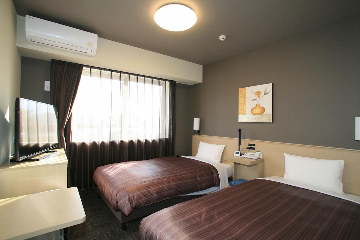 A hotel room with two beds, a desk, a TV, an air conditioner, and a painting on the wall.