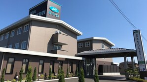 A modern hotel building with a prominent logo on the facade, a covered entrance, and a sign indicating a parking area. - Hotel Route Inn Natori Iwanuma Interchange (Iwanuma)