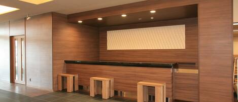 Una moderna zona de recepción con un mostrador de madera, tres taburetes de madera y un ventanal con persianas.