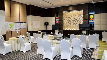 A conference room with round tables, white chairs, and a projector screen.