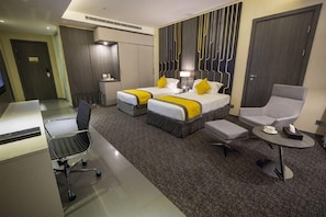 A hotel room with two beds, a desk, a chair, and a small table.