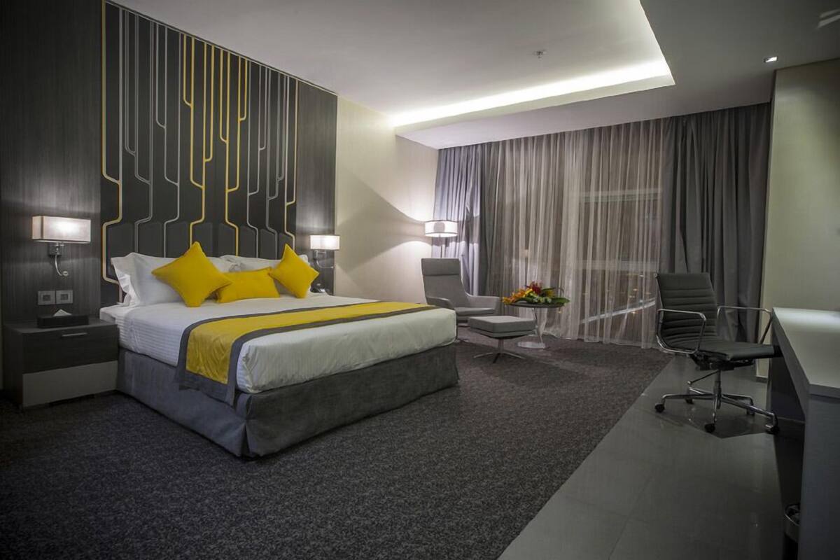 A modern hotel room with a large bed, a desk, a chair, and a small table with a vase of flowers.