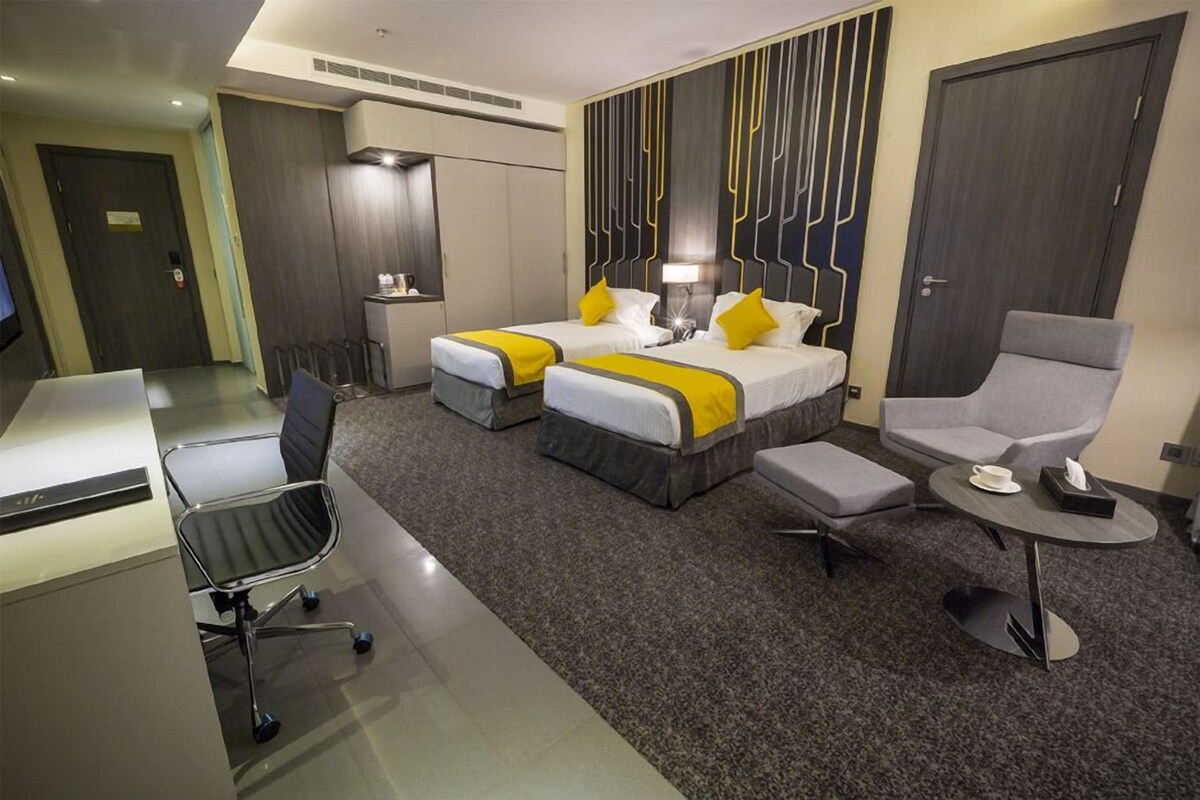 A hotel room with two beds, a desk, a chair, and a small table.