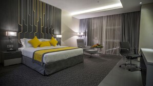 A modern hotel room with a large bed, a desk, a chair, and a small table with a vase of flowers. - Executives Hotel Kafd (Riyadh)