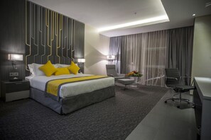 Une chambre d’hôtel moderne, dotée d’un grand lit, d’un bureau, d’une chaise et d’une petite table sur laquelle est posé un vase de fleurs.