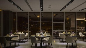 A modern dining area with tables and chairs, large windows, and a city view at night. - Executives Hotel Kafd (Riyadh)