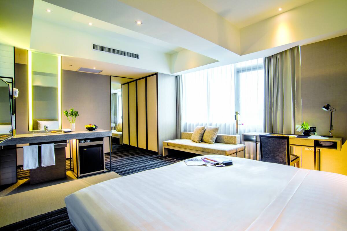A modern hotel room with a large bed, a desk, a seating area, and a bathroom.