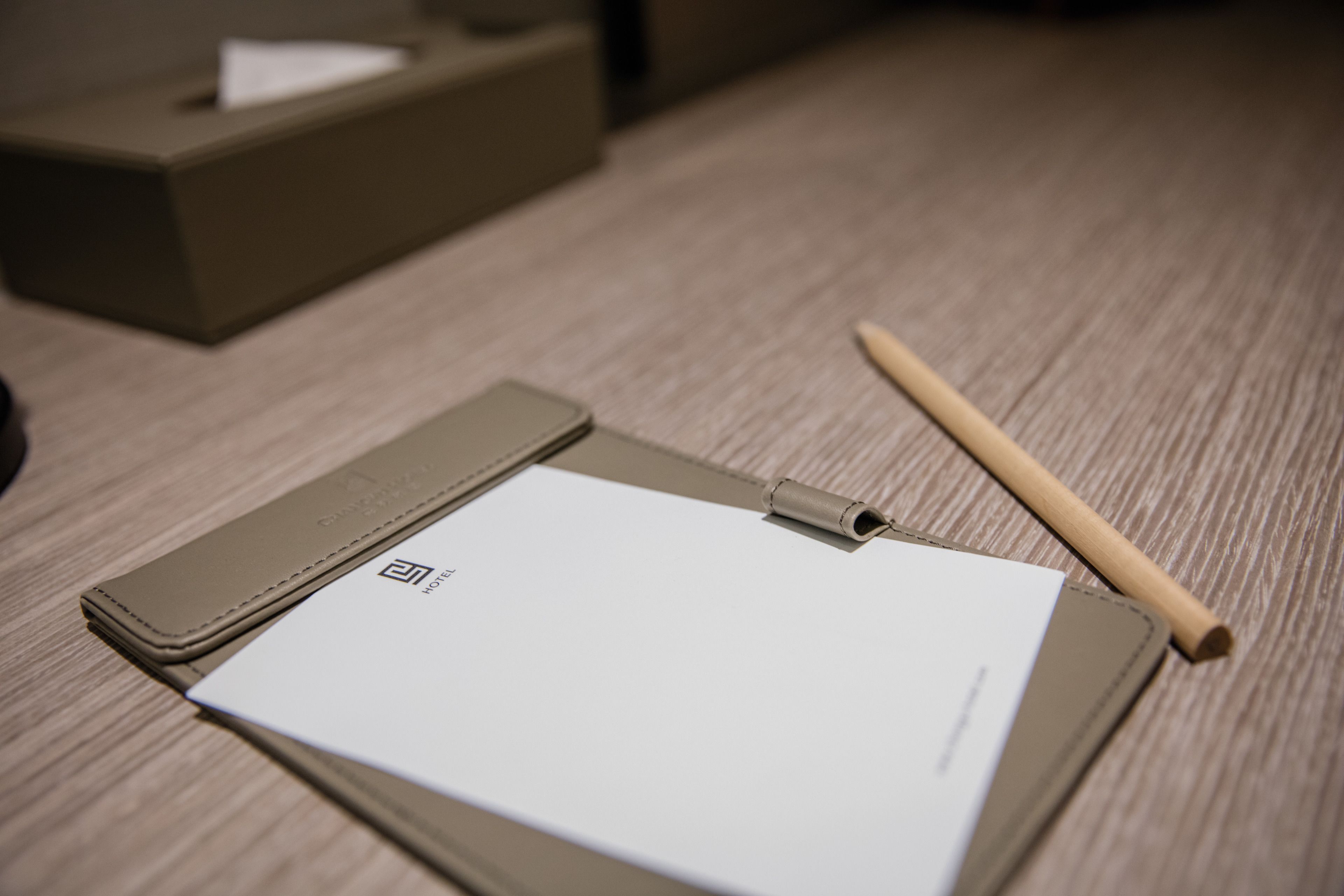 A hotel room with a wooden floor, a brown leather side table, a white notepad, a pen, and a tissue box.