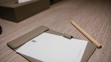 A hotel room with a wooden floor, a brown leather side table, a white notepad, a pen, and a tissue box.