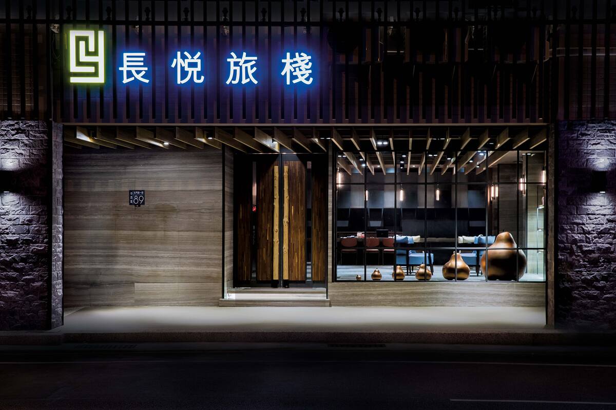 A modern hotel entrance with a neon sign, wooden facade, and a view of the interior through glass doors.