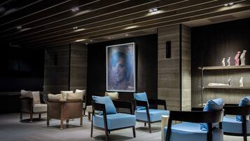 A modern lounge area with dark wood paneling, blue upholstered chairs, and a large digital art display.
