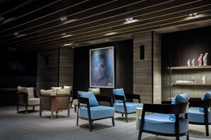 Ein moderner Loungebereich mit dunklen Holzpaneelen, blau gepolsterten Sesseln und einer großen digitalen Kunstausstellung.