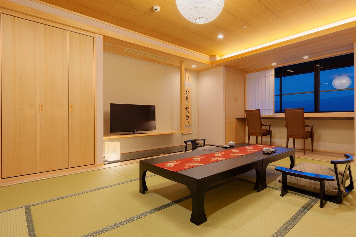 A traditional Japanese room with tatami flooring, a low table, chairs, a television, and sliding doors.