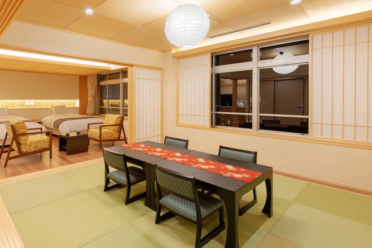 A traditional Japanese-style room with tatami flooring, a low table with a red table runner, and shoji screens.