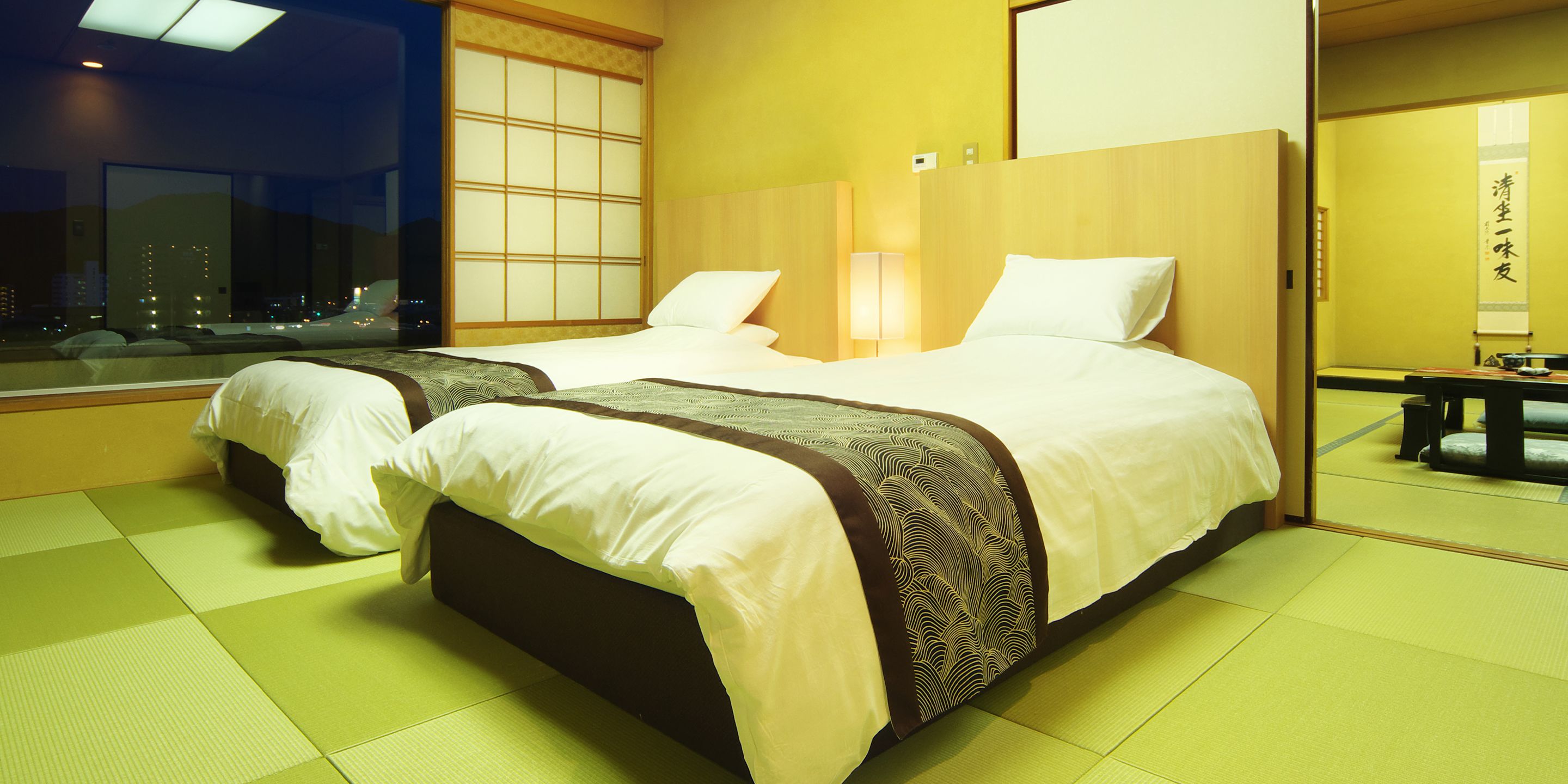 Habitación de hotel con dos camas, un ventanal grande y una puerta corrediza tradicional japonesa.