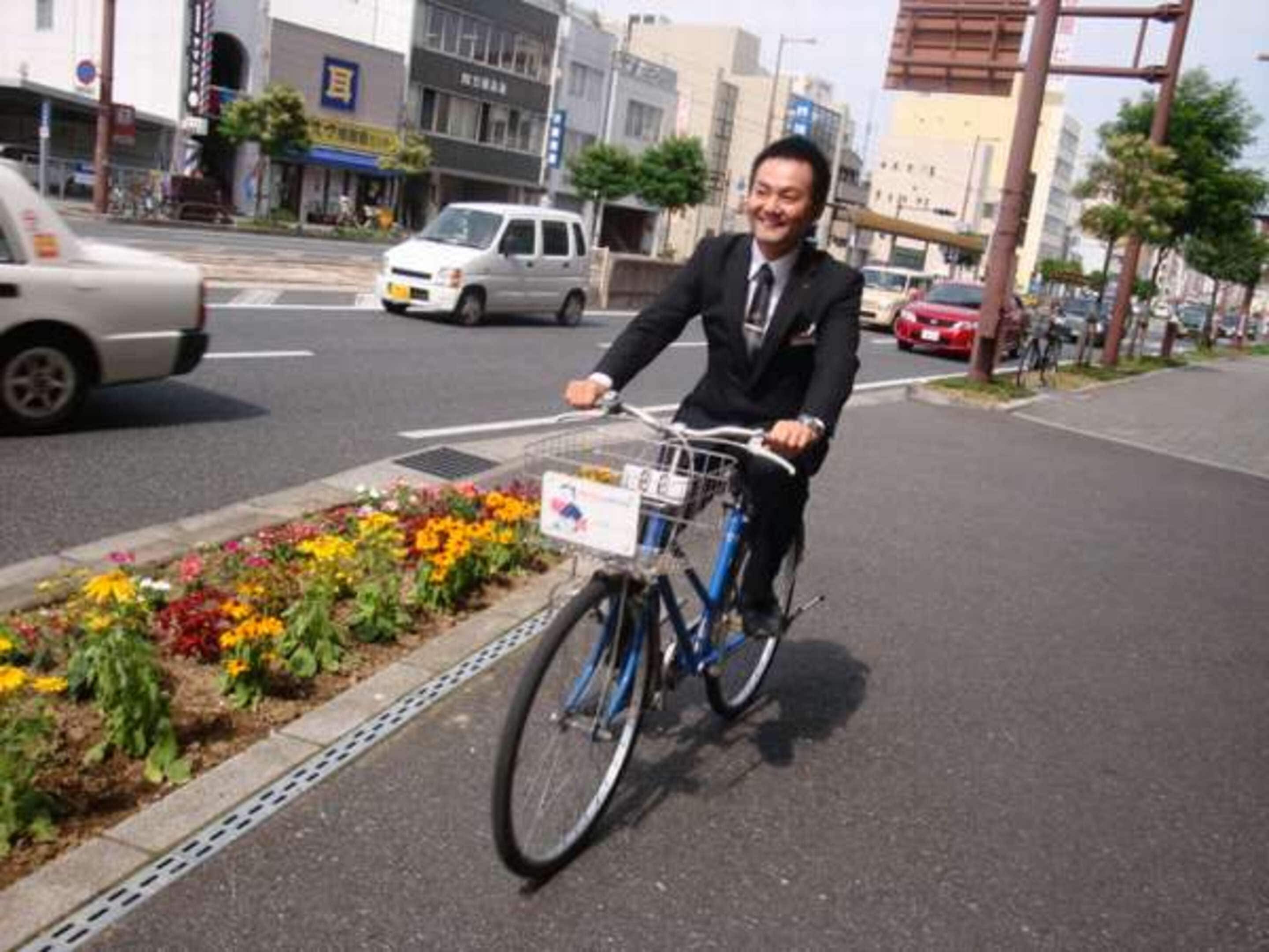 Eine Person fährt Fahrrad auf einer Stadtstraße, an deren Seite ein Blumenbeet liegt.