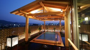 A rooftop pool area with wooden pergolas and potted plants, overlooking a cityscape at dusk. - Jyoseikan (Kochi)