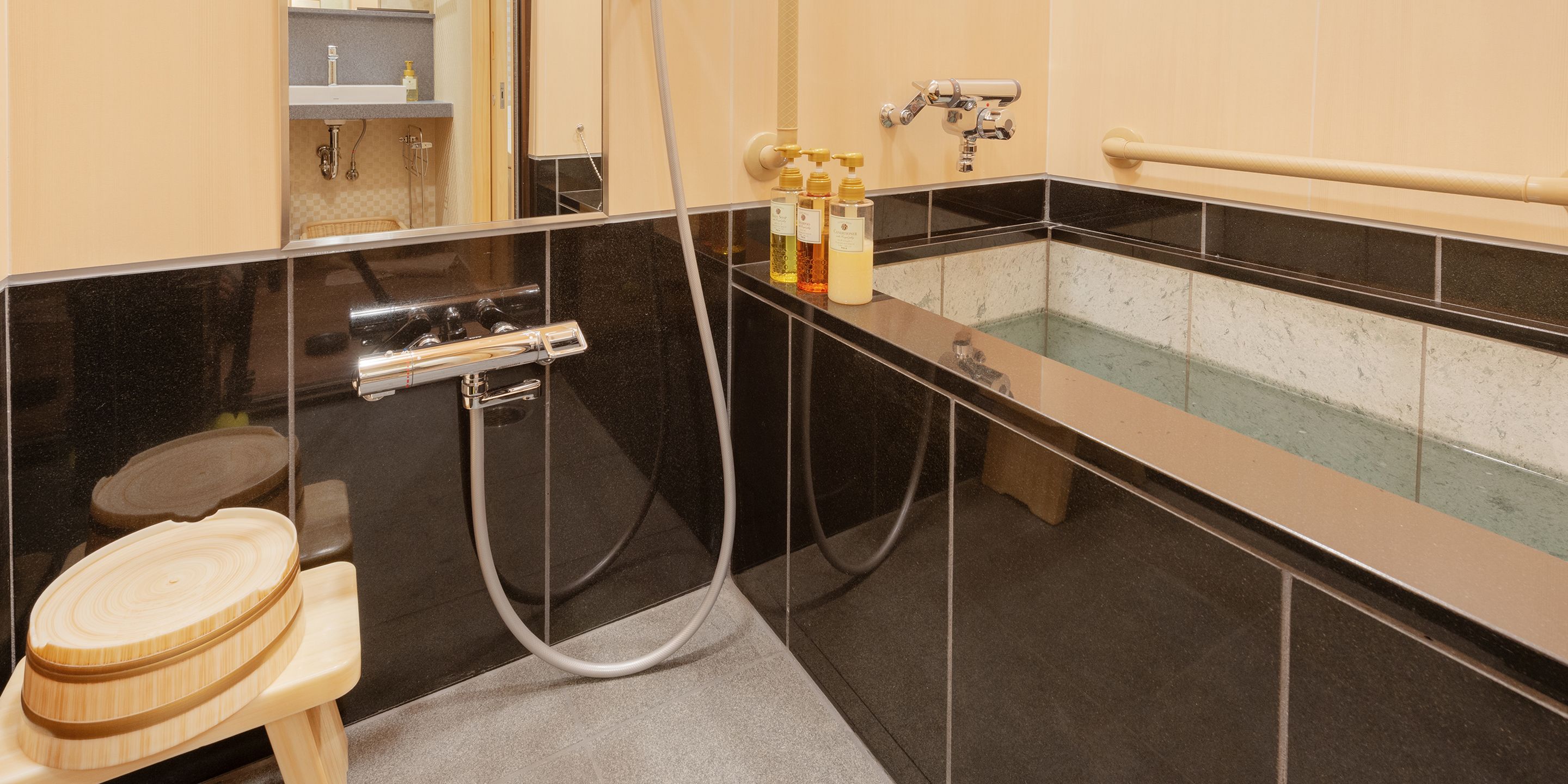 Un baño moderno con una paleta de colores negro y beige, una bañera, un inodoro y un taburete de madera.