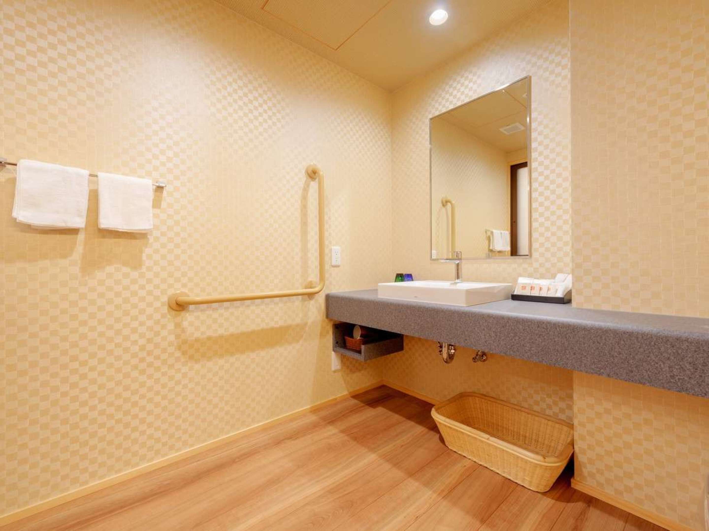 Un baño con un estampado de cuadros en la pared, un lavabo con espejo, un perchero, un asidero, una cesta y un estante pequeño con artículos de aseo.