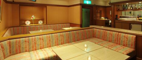 A hotel lobby with a large, striped booth seating area, a bar with a counter and shelves of bottles, and a television mounted on the wall.