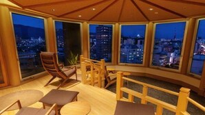 A high-rise room with a panoramic city view, furnished with wooden chairs and tables, and a wooden railing. - Jyoseikan (Kochi)