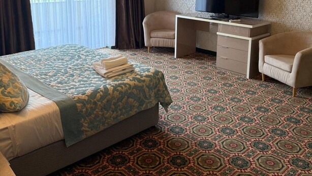 Habitación de hotel con cama, escritorio con televisor, dos sillas y alfombra estampada.