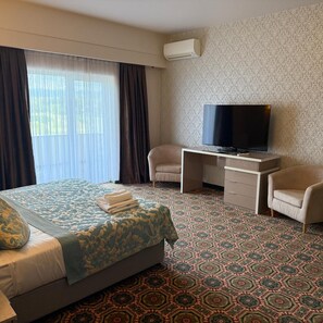 Habitación de hotel con cama, escritorio con televisor, dos sillas y alfombra estampada.