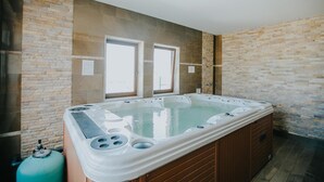 Un amplio jacuzzi interior con base de madera, frente a una pared de piedra con dos ventanas.