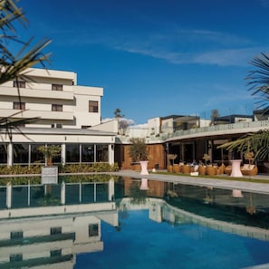 A modern hotel with a pool, outdoor seating, and a clear blue sky. - Hotel Romanita (Baia Mare)