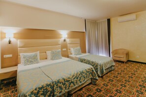 Ein Hotelzimmer mit zwei Betten, einem Sessel, einem gemusterten Teppich und einem Vorhang.