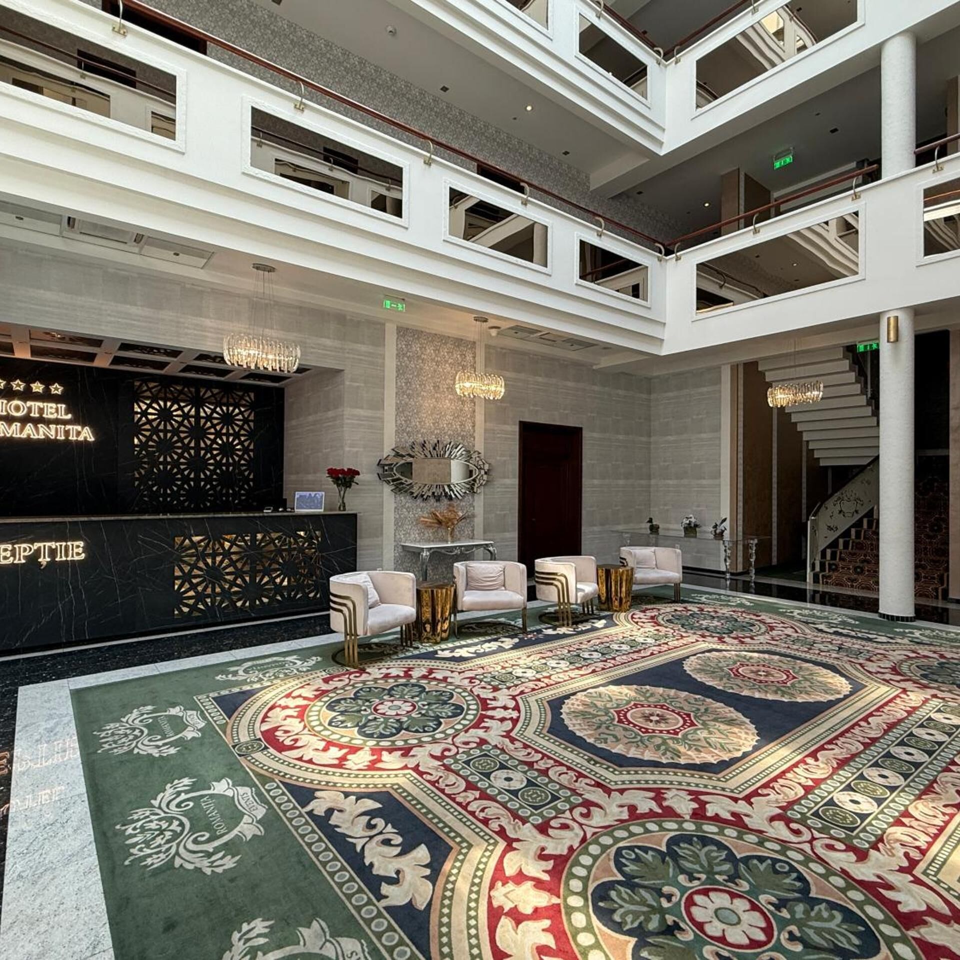 A hotel lobby with a reception desk, seating area, chandeliers, and a patterned carpet.