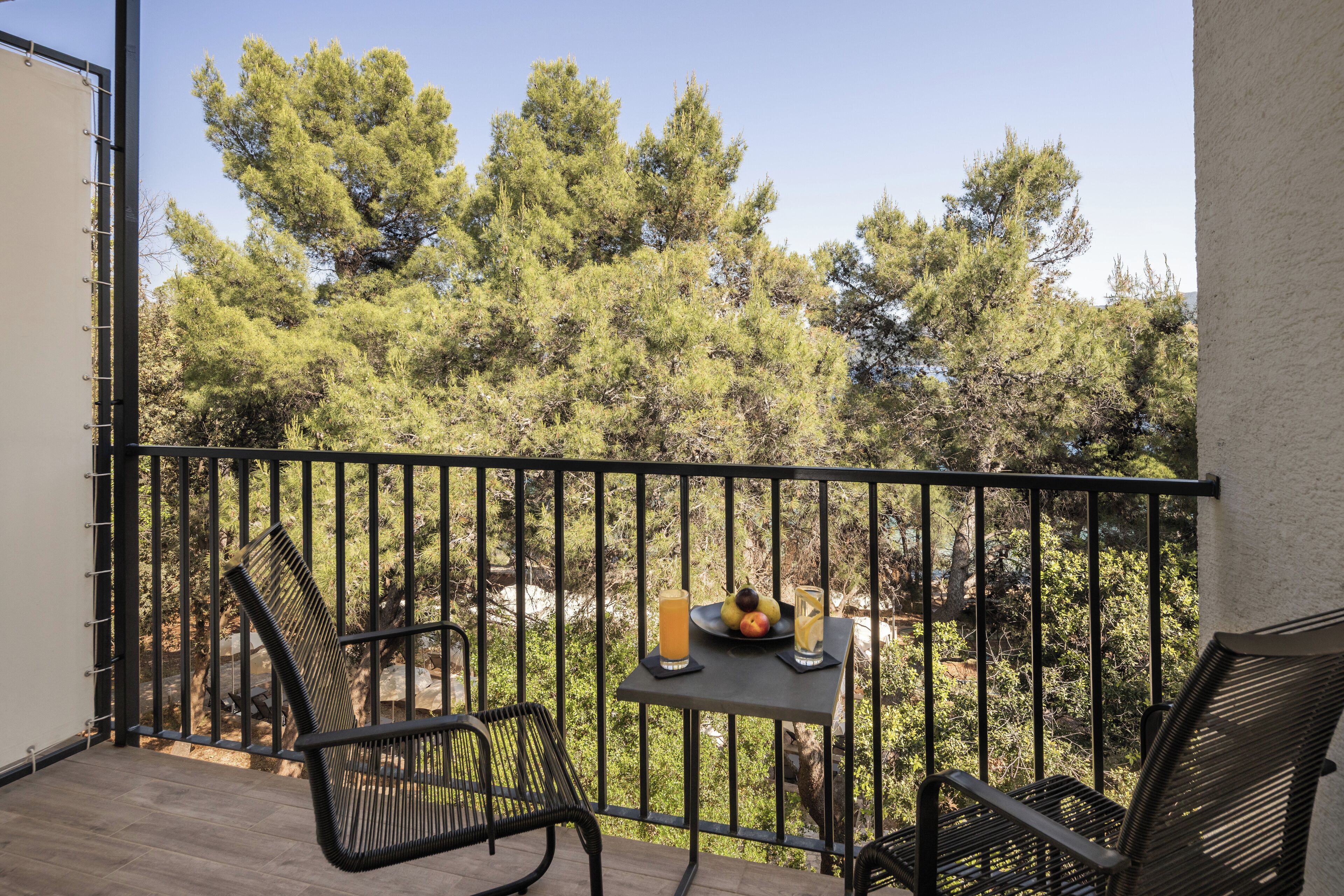 A balcony with a table set for two, featuring a fruit plate, a glass of orange juice, and a glass of water.