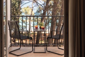 A balcony with two chairs and a table, a potted plant, and a view of trees and sky.