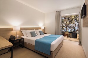 A hotel room with a bed, a desk, a chair, a TV, and a balcony with outdoor seating.