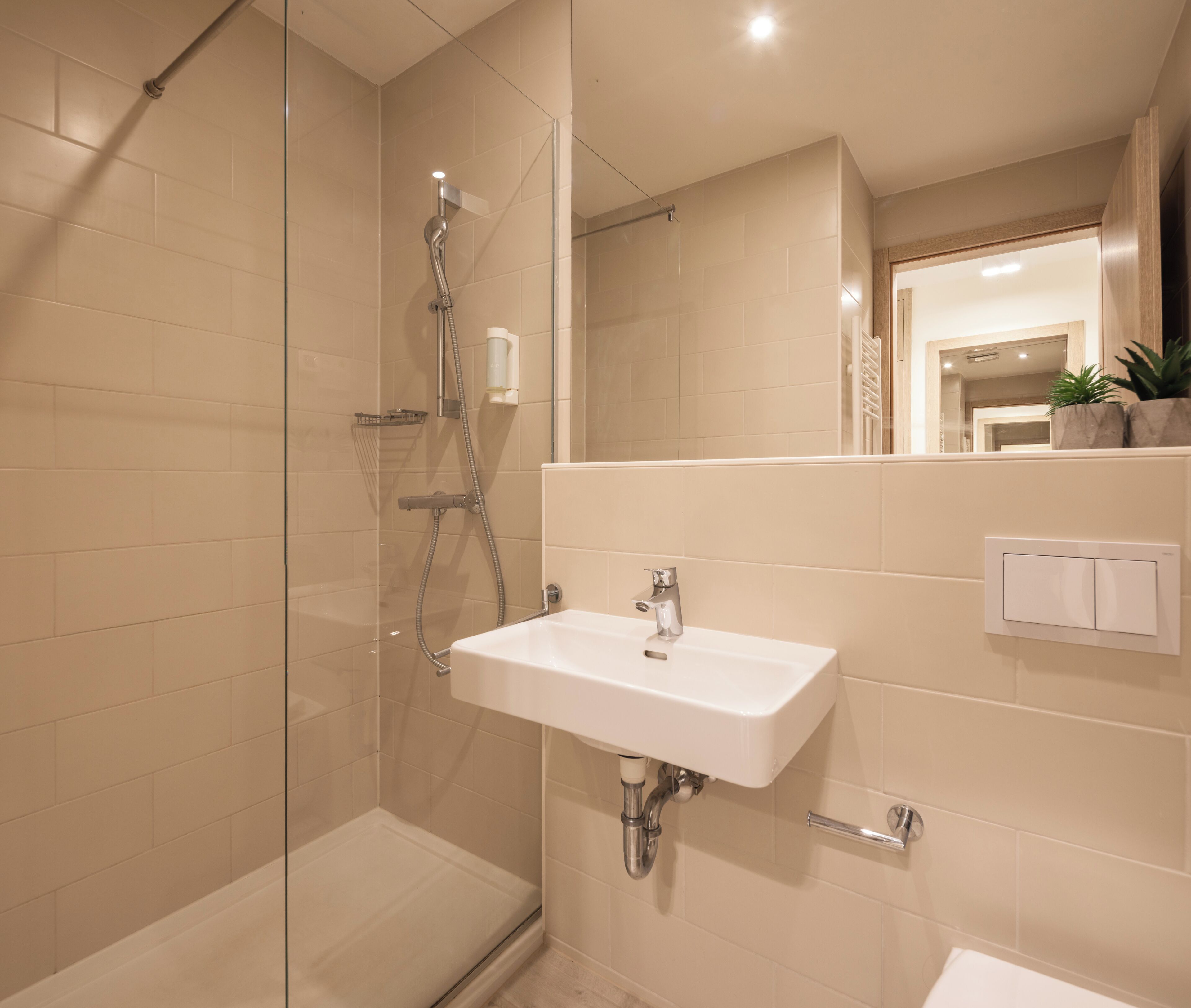 Une salle de bain moderne avec une douche à parois de verre, un lavabo blanc et un miroir qui reflète la pièce.