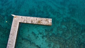 An aerial view of a rectangular pier extending into clear turquoise water, with a tiled walkway and a rope for safety.