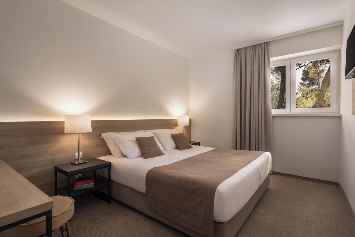 A hotel room with a bed, bedside table, lamp, and a window with curtains.