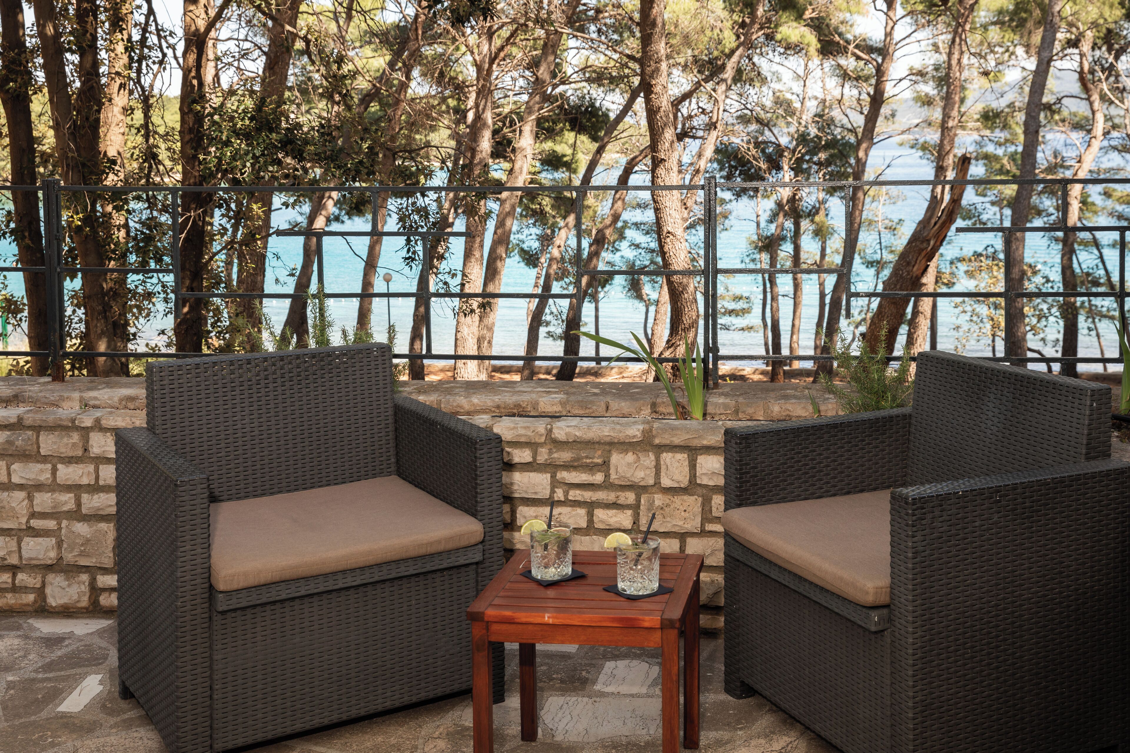 A patio area with wicker furniture and a small table, overlooking a body of water and trees.