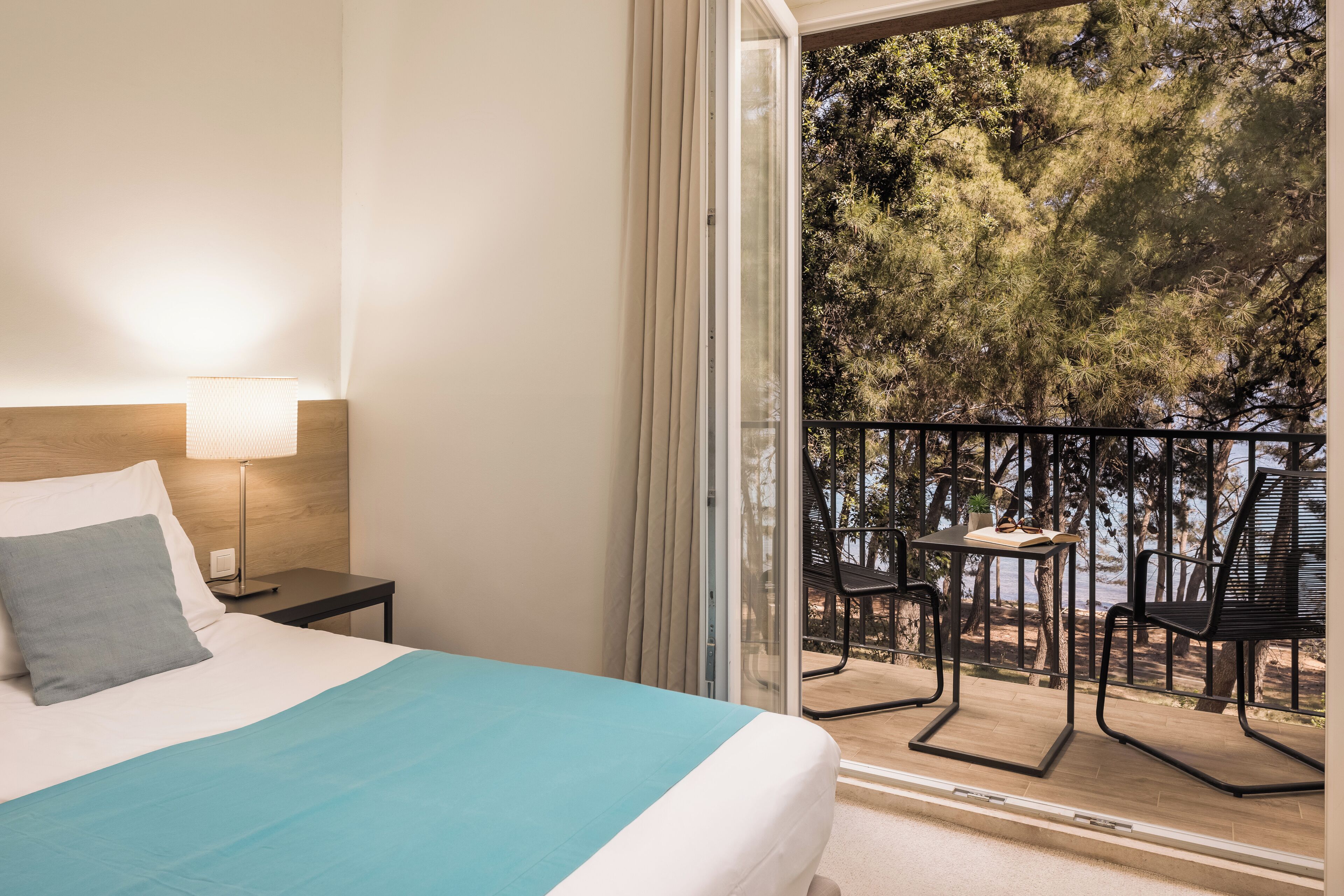 Une chambre à coucher comprenant un lit, une table de chevet, une lampe et un balcon avec des chaises et une table.