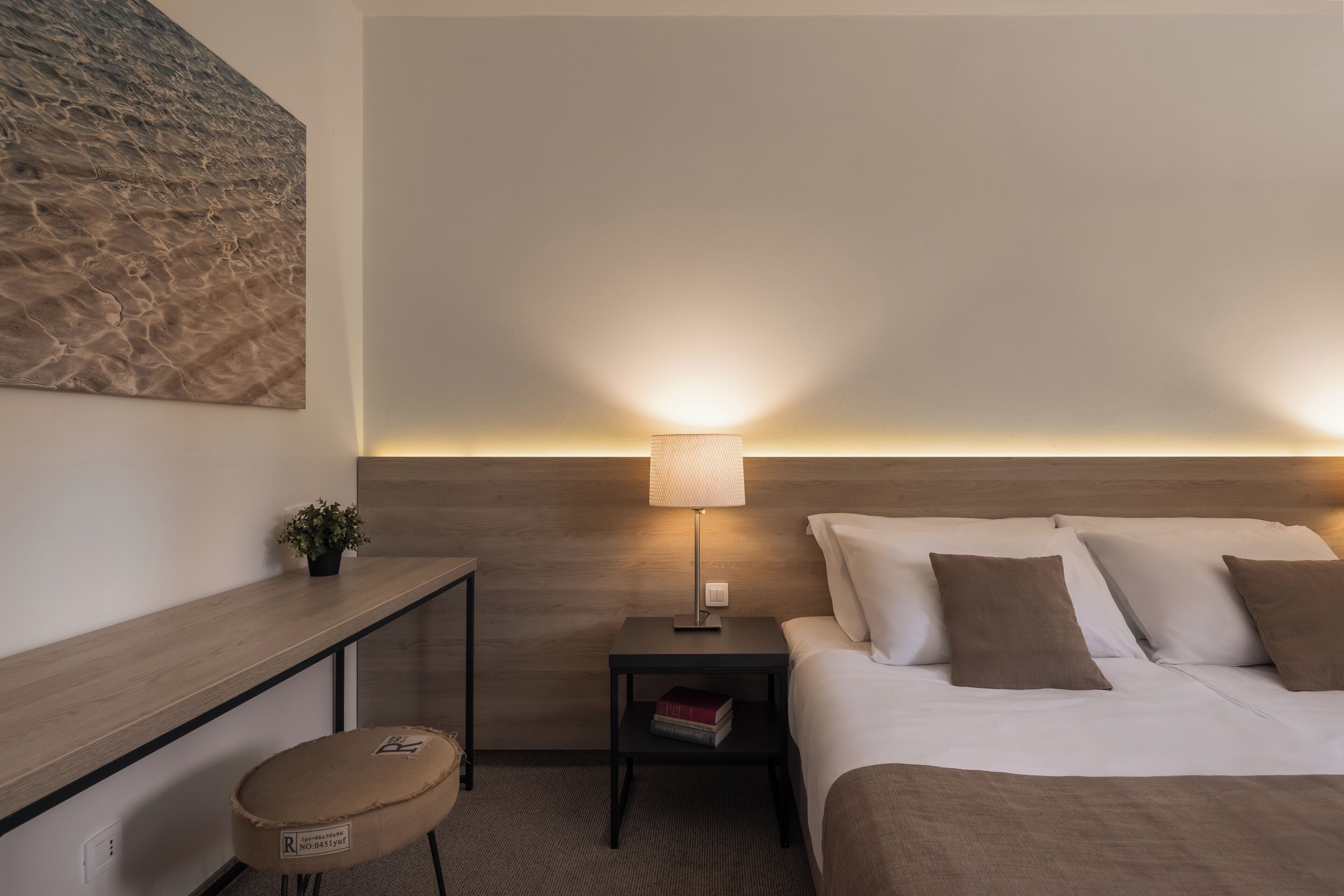 Ein Hotelzimmer mit Bett, Nachttisch, Lampe und einem kleinen Hocker.