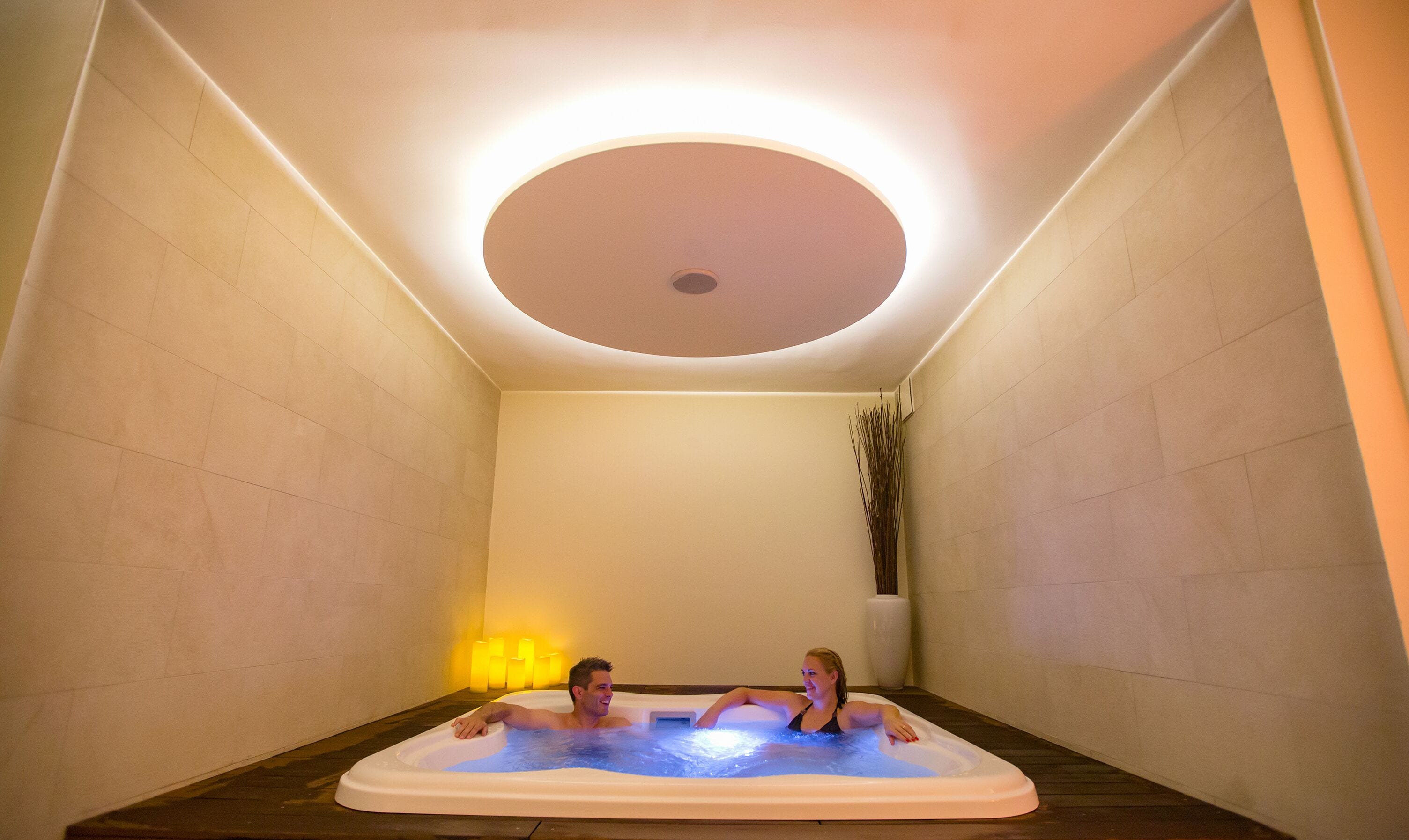 A spa room with a hot tub, a ceiling light, and a vase with plants.